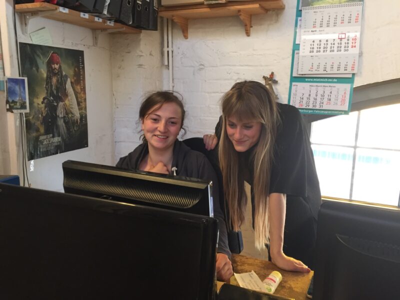 Zwei junge Mitarbeiterinnen lachen gemeinsam am Schreibtisch im Büro der Waggonhalle