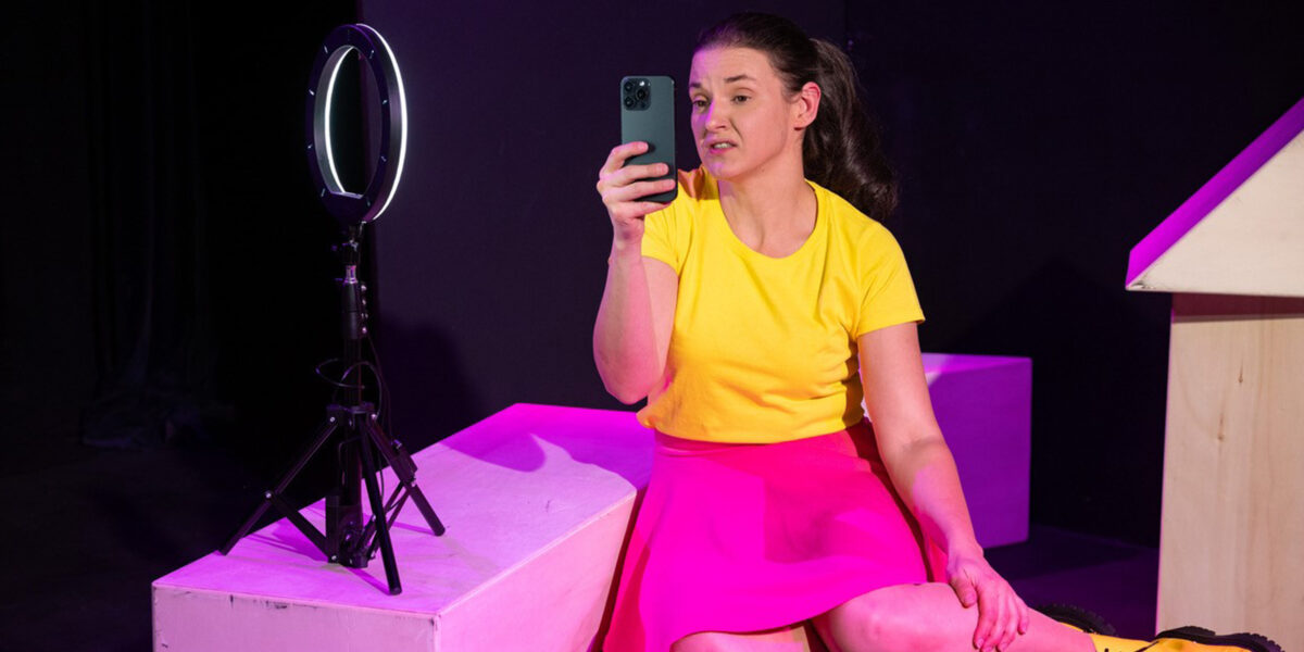 Eine Frau filmt sich mit dem Handy. Sie hat ein gelbes T-Shirt und einen rosa Rock an. Links ein Ringlicht wie ihn Influencer benutzen.